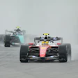 Formula 1 racing cars competing on a wet track in rainy conditions, with red and black vehicles leading the field.