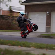 Stunt rider performing wheelie on red motorcycle in residential neighborhood street