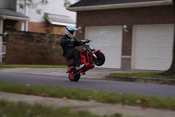 Stunt rider performing wheelie on red motorcycle in residential neighborhood street