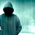 Hooded figure silhouette with digital binary code overlay on teal background representing cybersecurity and hacking