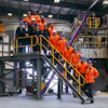 Industrial facility tour with group in orange safety uniforms on yellow metal stairs and platforms