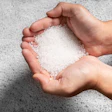 Hands holding white salt or sugar crystals against concrete background