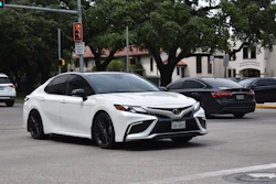 White Toyota Camry sedan parked on urban street with trees and buildings in background