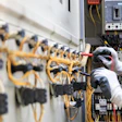 Electrician installing yellow wiring in industrial circuit breaker panel with safety gloves