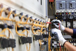 Electrician installing yellow wiring in industrial circuit breaker panel with safety gloves