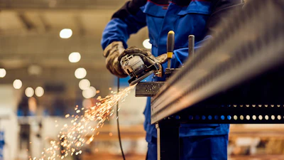 Industrial worker in blue uniform using angle grinder on metal with sparks flying in factory setting