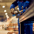 Industrial worker in blue uniform using angle grinder on metal with sparks flying in factory setting