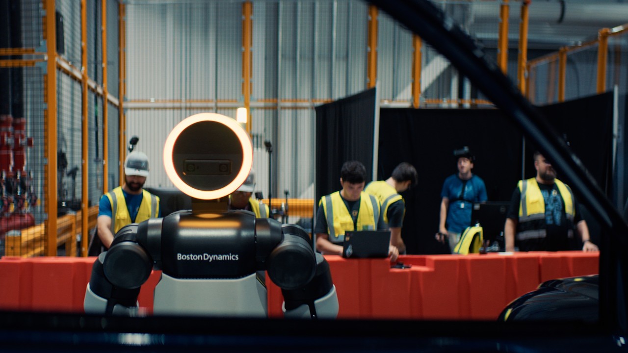 Boston Dynamics robot Spot with glowing head ring displayed at industrial facility with workers in safety vests observing