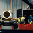 Boston Dynamics robot Spot with glowing head ring displayed at industrial facility with workers in safety vests observing