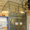 Industrial safety cage with mesh panels and yellow-black striping in warehouse facility