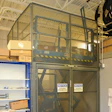 Industrial safety cage with mesh panels and yellow-black striping in warehouse facility