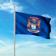 Michigan state flag waving on a flagpole against a blue sky with white clouds