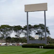 Large blank billboard with metal frame in commercial area surrounded by trees, buildings, and parked vehicles