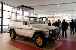 Vintage Mercedes-Benz G-Class with white body and gold wheels displayed in modern showroom with visitors