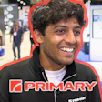 Smiling man wearing PRIMARY branded black jacket at indoor event or trade show