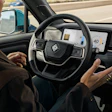 Driver with hands on steering wheel inside modern autonomous vehicle with digital dashboard display