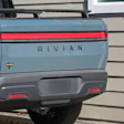 Rear view of light blue Rivian R1T electric truck with red horizontal tail lights and gray bumper