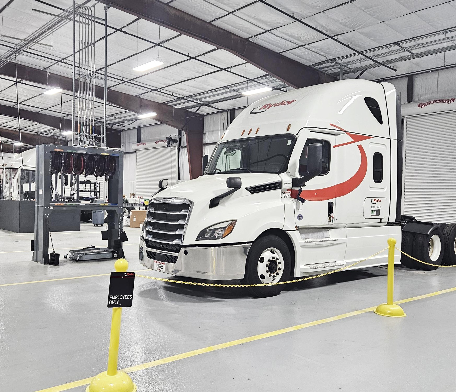 White Schneider semi-truck with red stripe parked in industrial warehouse facility with yellow safety barriers
