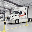 White Schneider semi-truck with red stripe parked in industrial warehouse facility with yellow safety barriers