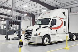 White Schneider semi-truck with red stripe parked in industrial warehouse facility with yellow safety barriers