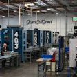 Industrial manufacturing facility with blue CNC machines and Sena CutSend signage on warehouse wall