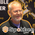 Man speaking at Spokbee corporate event with branded backdrop and logo watermark