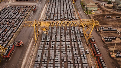 Aerial view of busy shipping port with hundreds of stacked containers, yellow gantry cranes, and cargo handling equipment