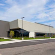 Modern industrial building with metal siding, glass entrance, and manicured landscaping under blue sky