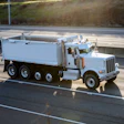 White Peterbilt dump truck traveling on a multi-lane highway with grassy hillside in background