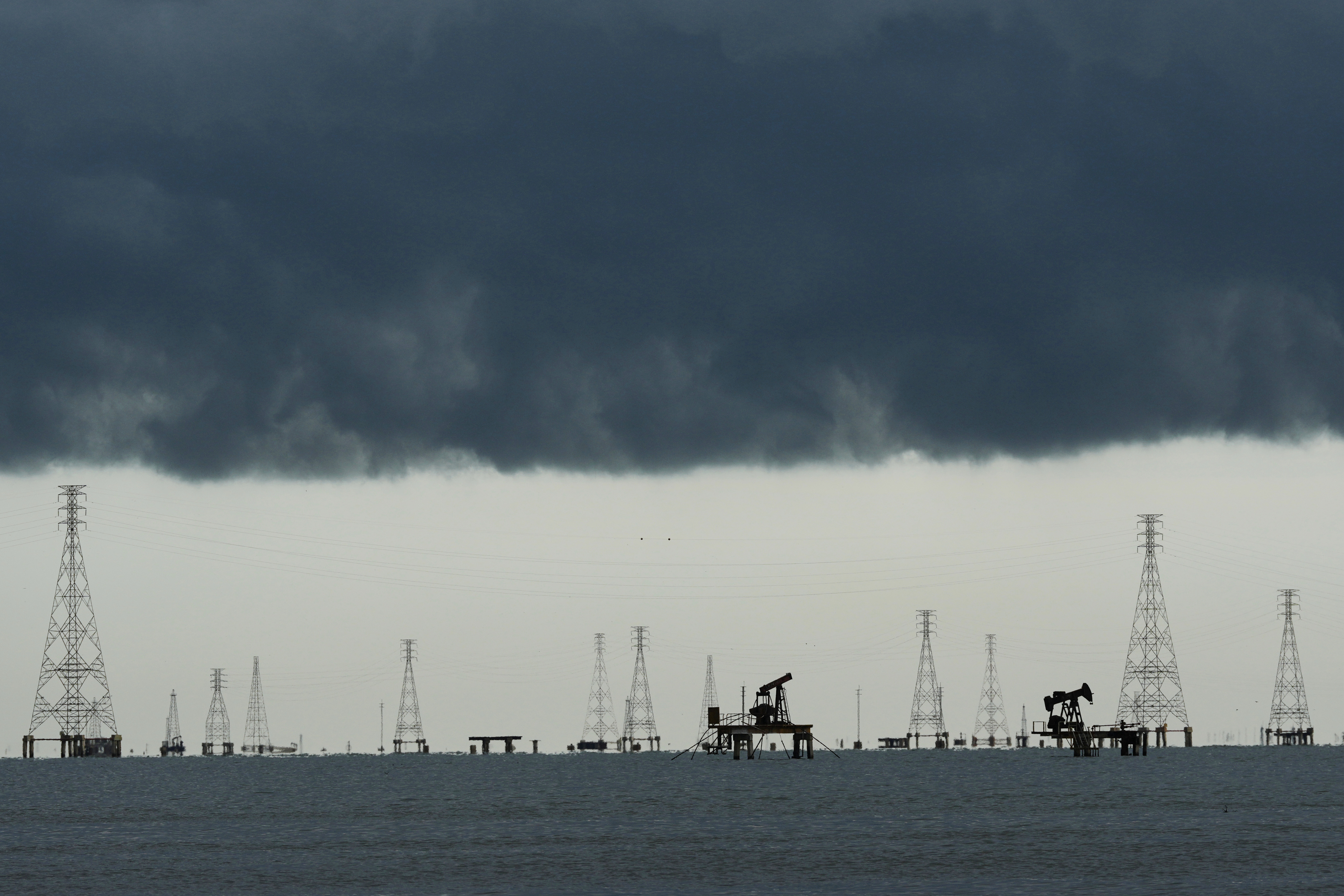 Offshore oil and gas extraction platform with multiple derricks and pump jacks silhouetted against dark storm clouds