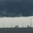 Offshore oil and gas extraction platform with multiple derricks and pump jacks silhouetted against dark storm clouds
