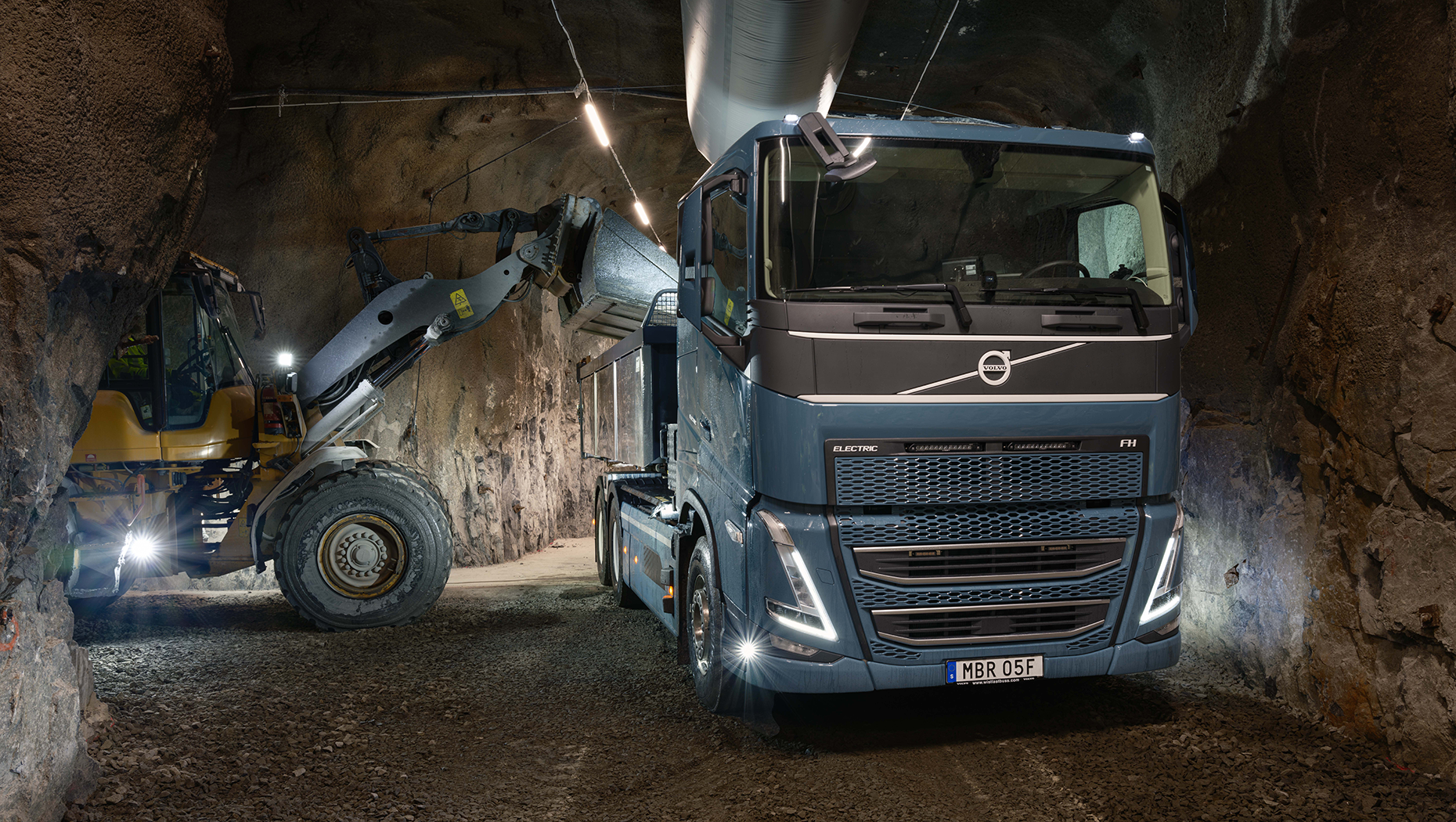 Volvo truck and wheel loader operating in an underground tunnel construction site with bright LED lighting
